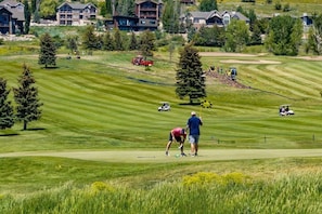 A golf course with a well-maintained green, a clubhouse, and residential buildings in the background.