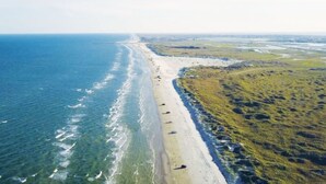 An aerial view of a beach with a long stretch of sand, a clear blue ocean, and some vegetation on the right side. - Howdy Holiday: Laguna Oasis (Corpus Christi)