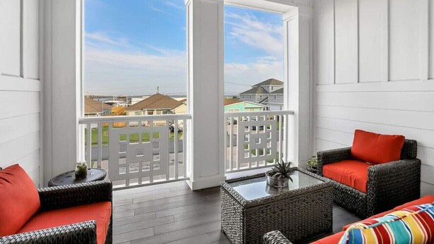 A balcony with wicker furniture, a small table, and a view of neighboring houses. - Howdy Holiday: Laguna Oasis (Corpus Christi)