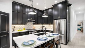 A modern kitchen with dark cabinets, stainless steel appliances, and a central island with bar stools. - Howdy Holiday: Laguna Oasis (Corpus Christi)