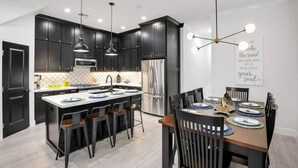 A modern kitchen with dark cabinetry, stainless steel appliances, and a central island with bar stools. - Howdy Holiday: Laguna Oasis (Corpus Christi)