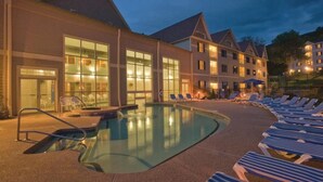 Un hotel con piscina, sillas de descanso y un exterior bien iluminado al anochecer.