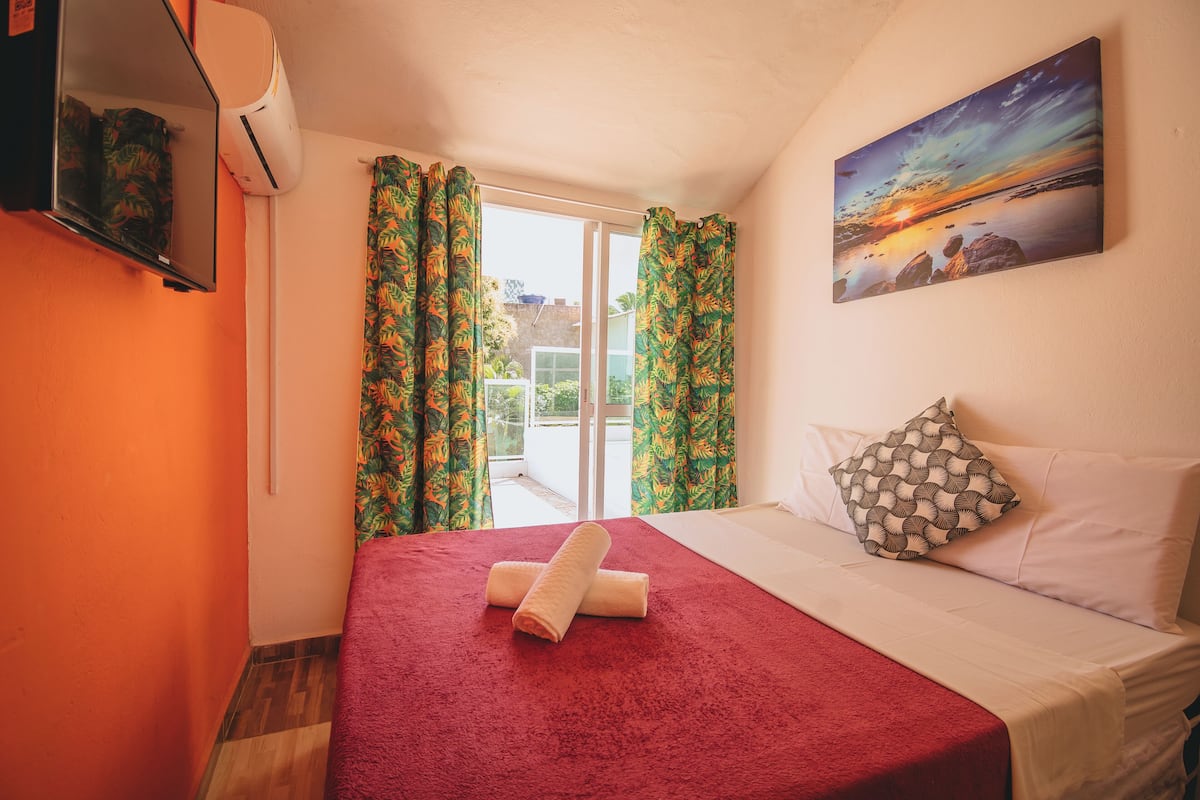 Habitación de hotel con cama, televisión montada en la pared y una pintura de un atardecer.