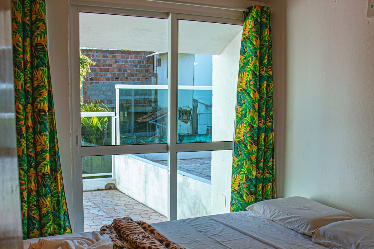 Un dormitorio con cama, ventana con cortinas y vistas al exterior.