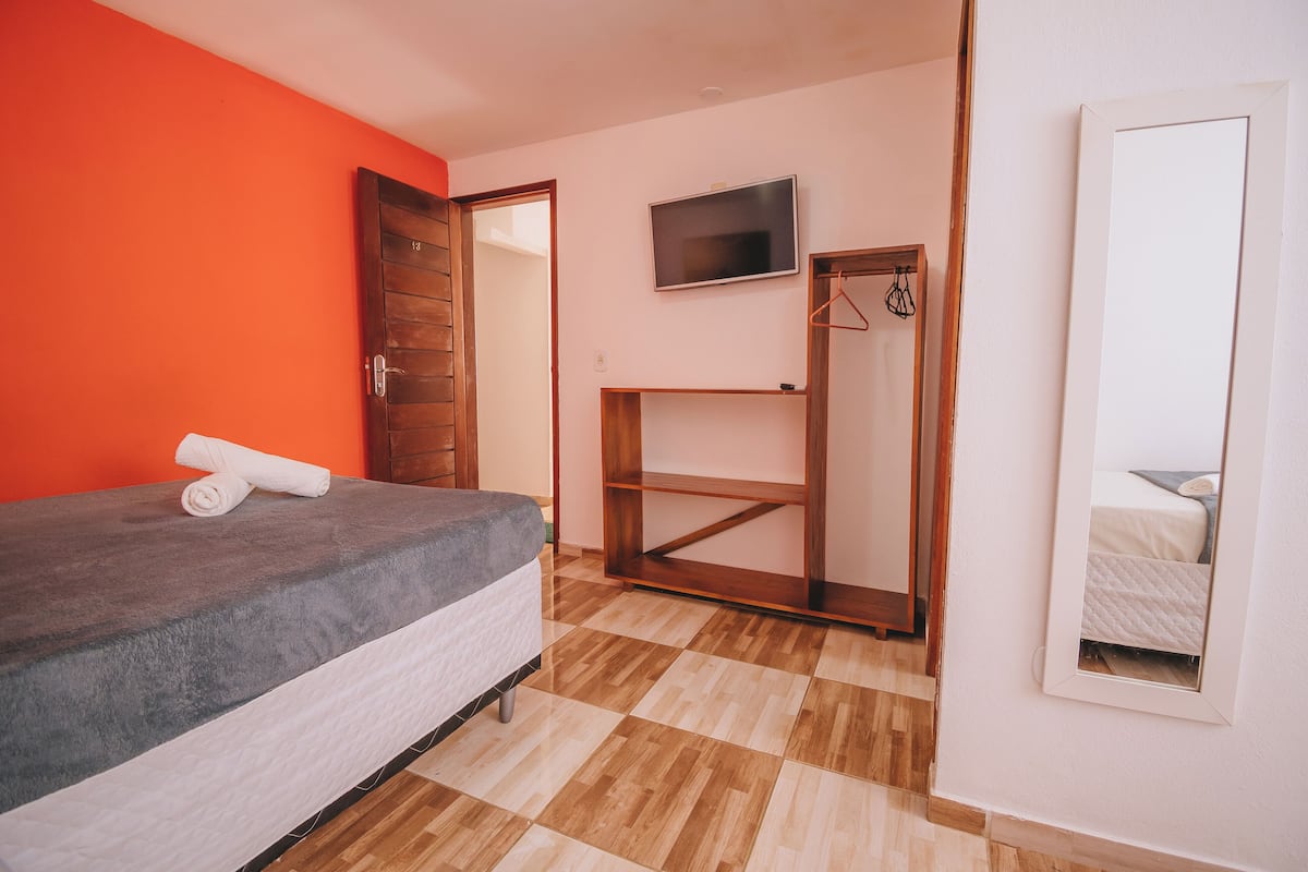 Un dormitorio con cama, televisor, armario y espejo.