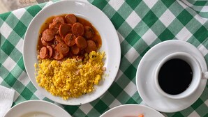 A table with a checkered tablecloth, plates of food, and a cup of coffee. - Pousada Porto  Amazônia (Ipojuca)