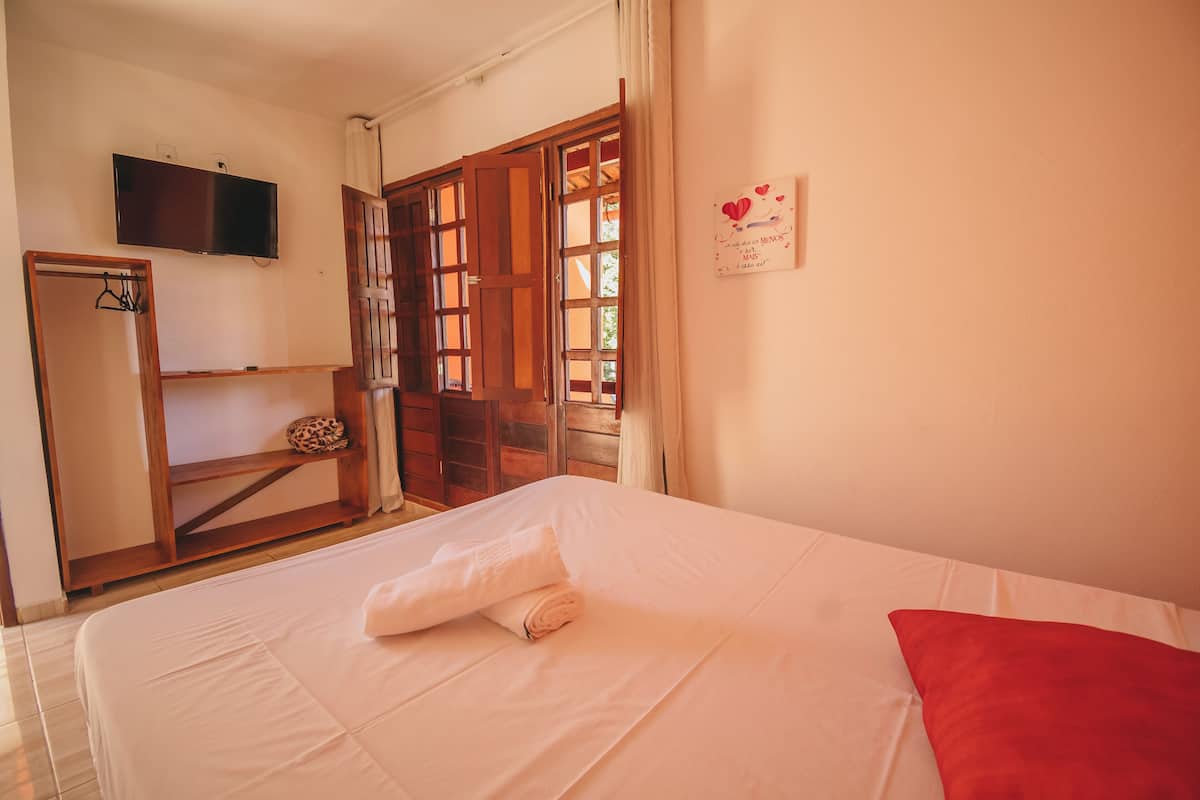 Una habitación de hotel con cama, televisor montado en la pared, armario y puerta que da al exterior.