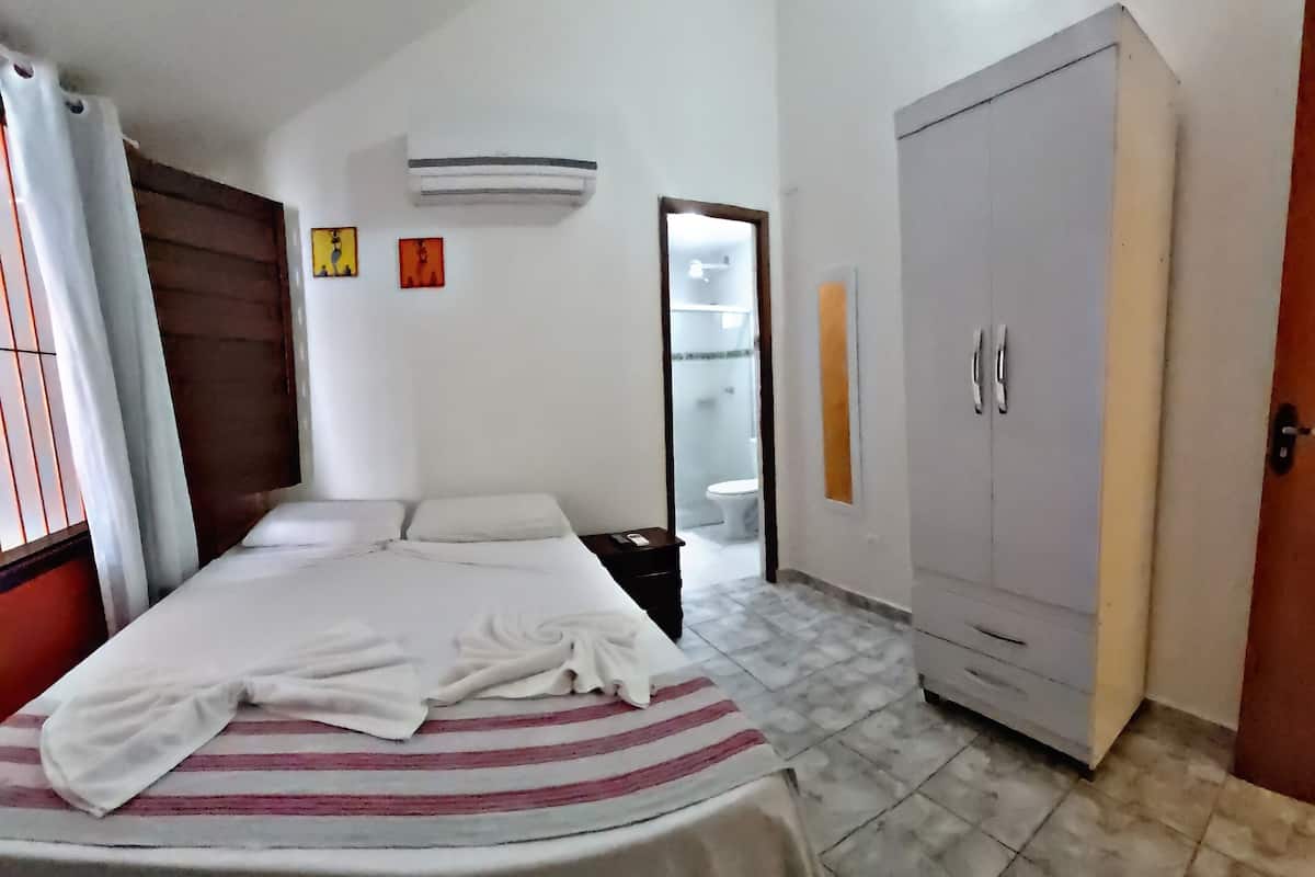 Un dormitorio con cama, armario, y baño a la vista a través de una puerta abierta, además de un aire acondicionado en la pared.