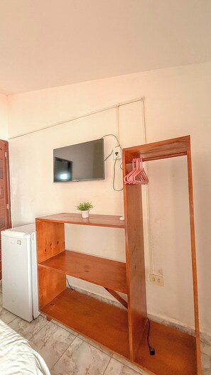 A compact room with a wooden desk, a small potted plant, and a television mounted on the wall. - Pousada Porto  Amazônia (Ipojuca)
