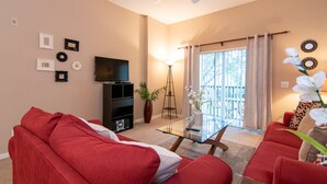 A living room with a red sofa, a glass coffee table, a TV, and a plant.