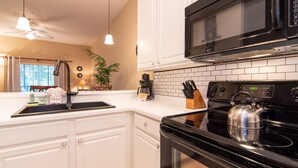 A kitchen with white cabinets, a black stove, a kettle, and a microwave.