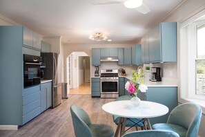 A modern kitchen with blue cabinets, stainless steel appliances, and a dining area with teal chairs. - Hudson Valley Hideaway - Heated Pool, Lake Access & Fenced Yard - Sleeps 8 (Copake)