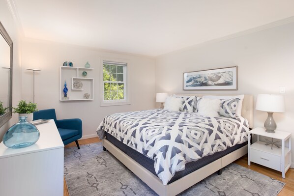 A modern bedroom with a bed, bedside tables, a chair, a desk, and a window.