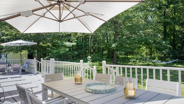 An outdoor patio with a white table, chairs, and a large umbrella.