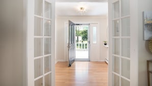A hallway with wooden flooring leading to a door with glass panels.