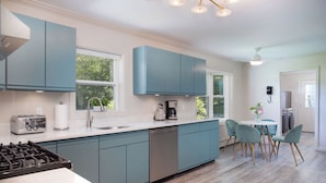 A modern kitchen with teal cabinets, a dishwasher, a gas stove, and a dining area with teal chairs.
