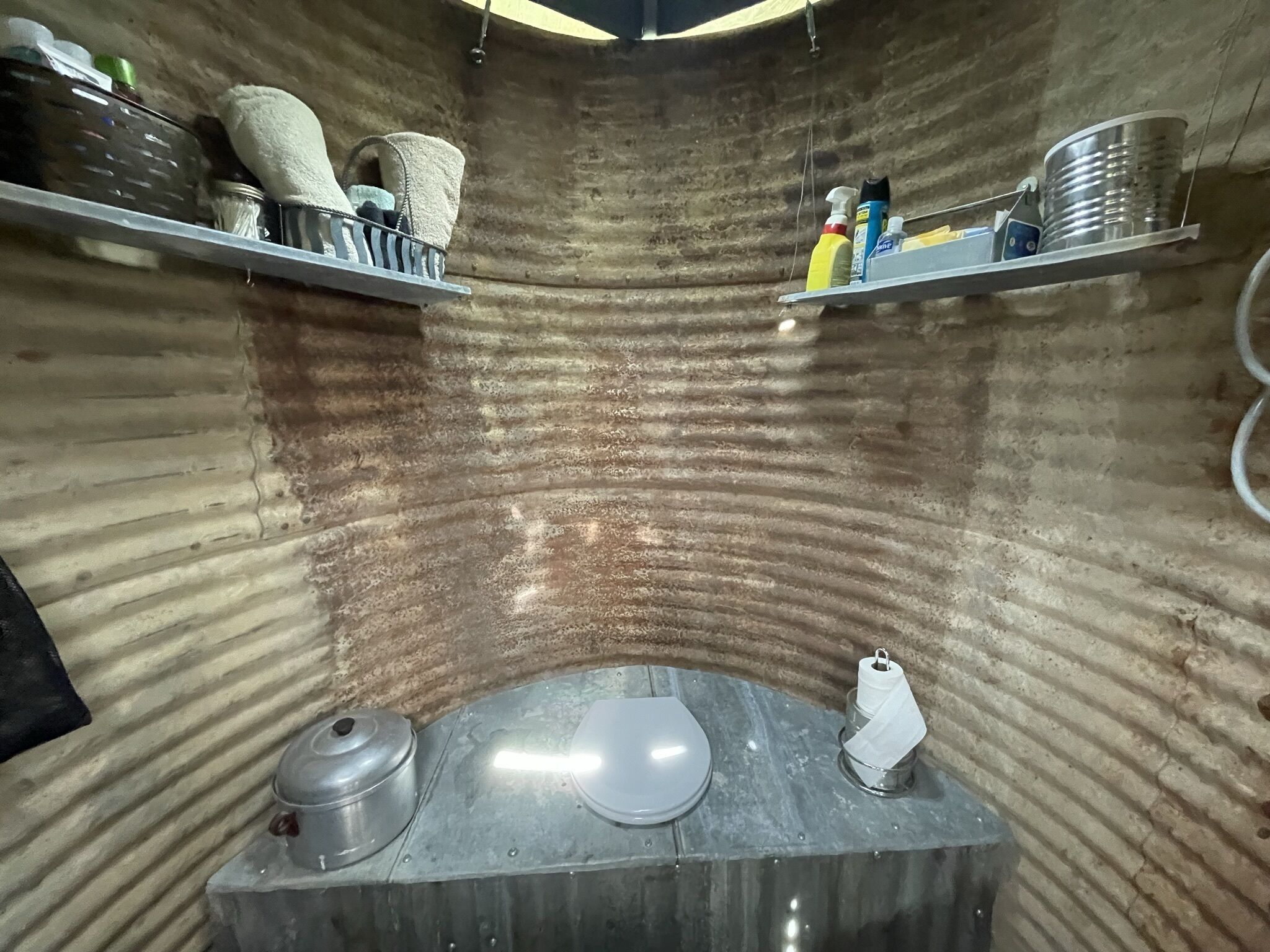 A compact, industrial-style bathroom with a curved wall design, metal fixtures, and storage shelves.