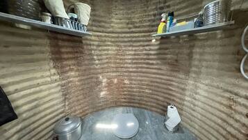A compact, industrial-style bathroom with a curved wall design, metal fixtures, and storage shelves.