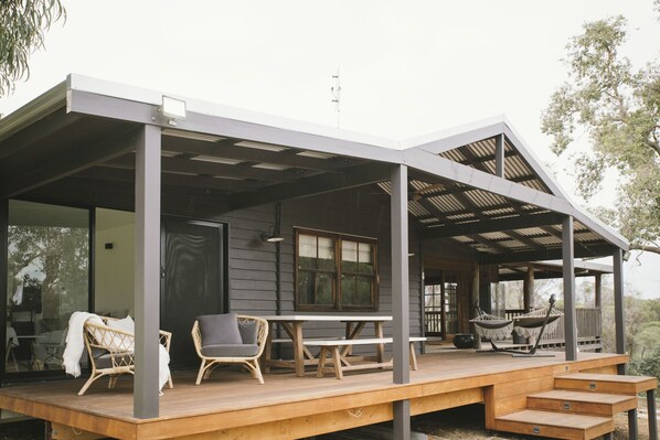 Un espace extérieur abrité, doté d'une terrasse en bois, de meubles en osier et d'une table.