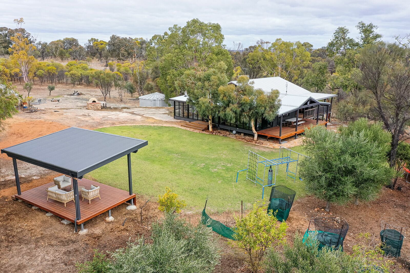 A spacious outdoor area with a covered seating area, a grassy lawn, and a large house with a deck and multiple windows.