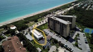 An aerial view of a coastal hotel with a large building, a parking lot, and a beach in the background. - Flirt with the Flamingos in Beach Bliss ~Just Steps to the Sand (FORT PIERCE)