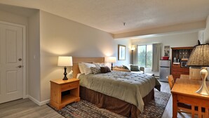 A bedroom with a bed, bedside table, lamp, and a view of the kitchen area. - Charming Studio Condo at Mt Green: Renovated, Steps to Mtn 3C13A (Killington)