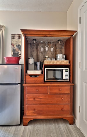 Una cocina con un mueble de madera que alberga un microondas, un hervidor y una olla roja en la parte superior.