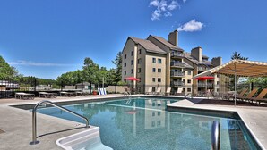 A swimming pool with a metal ladder, lounge chairs, and umbrellas.