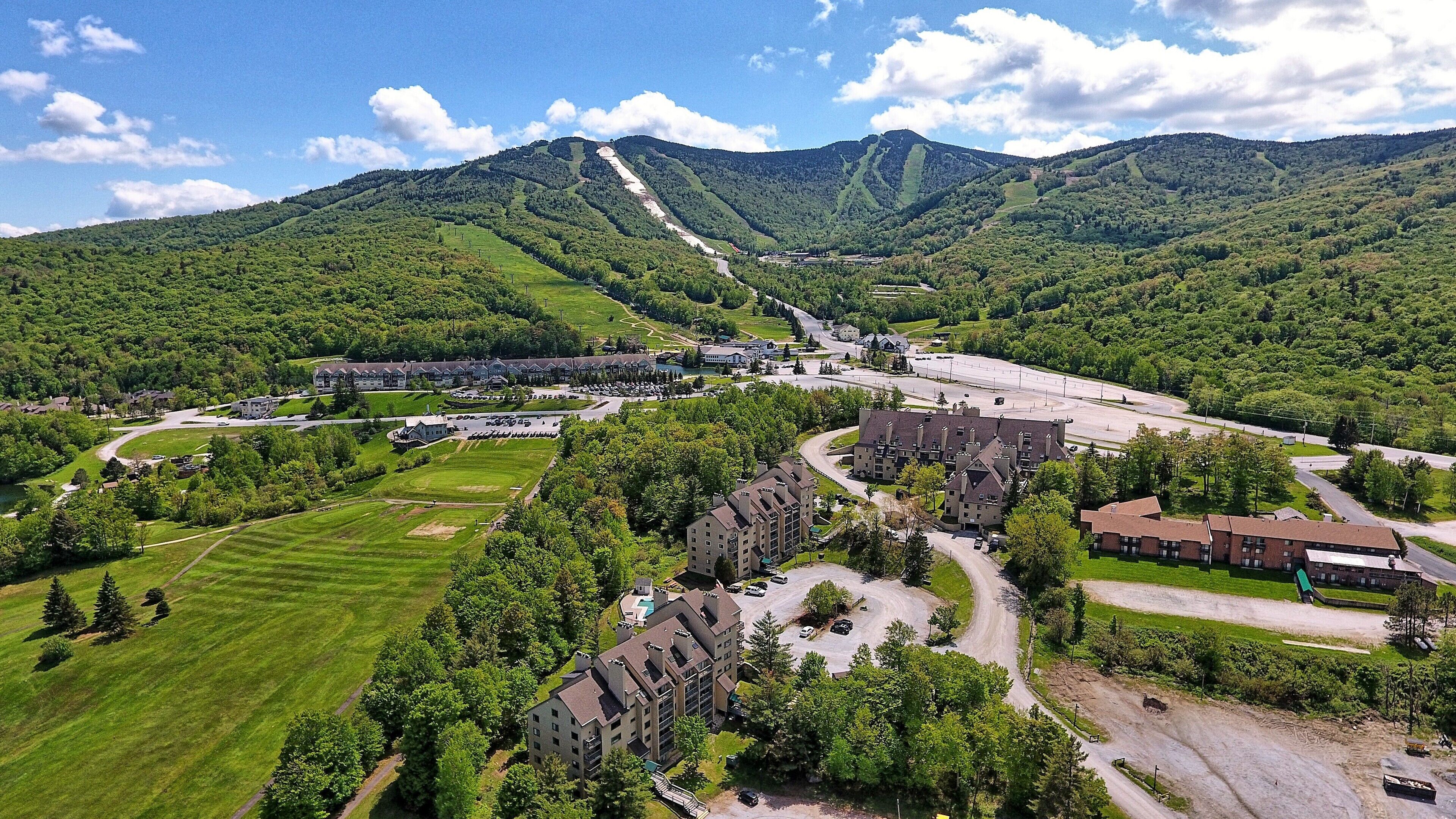 Un vaste complexe hôtelier comprenant plusieurs bâtiments, des aires de stationnement et un cadre montagneux pittoresque.