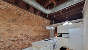 Una cocina con pared de ladrillo, vigas de madera, armarios blancos, estufa blanca y refrigerador blanco.