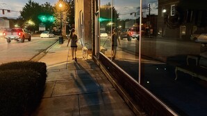 Acerado con un escaparate de vidrio que refleja vehículos y farolas.