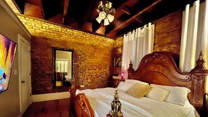Un dormitorio con cama de madera, paredes de ladrillo, ventilador de techo y un espejo grande.