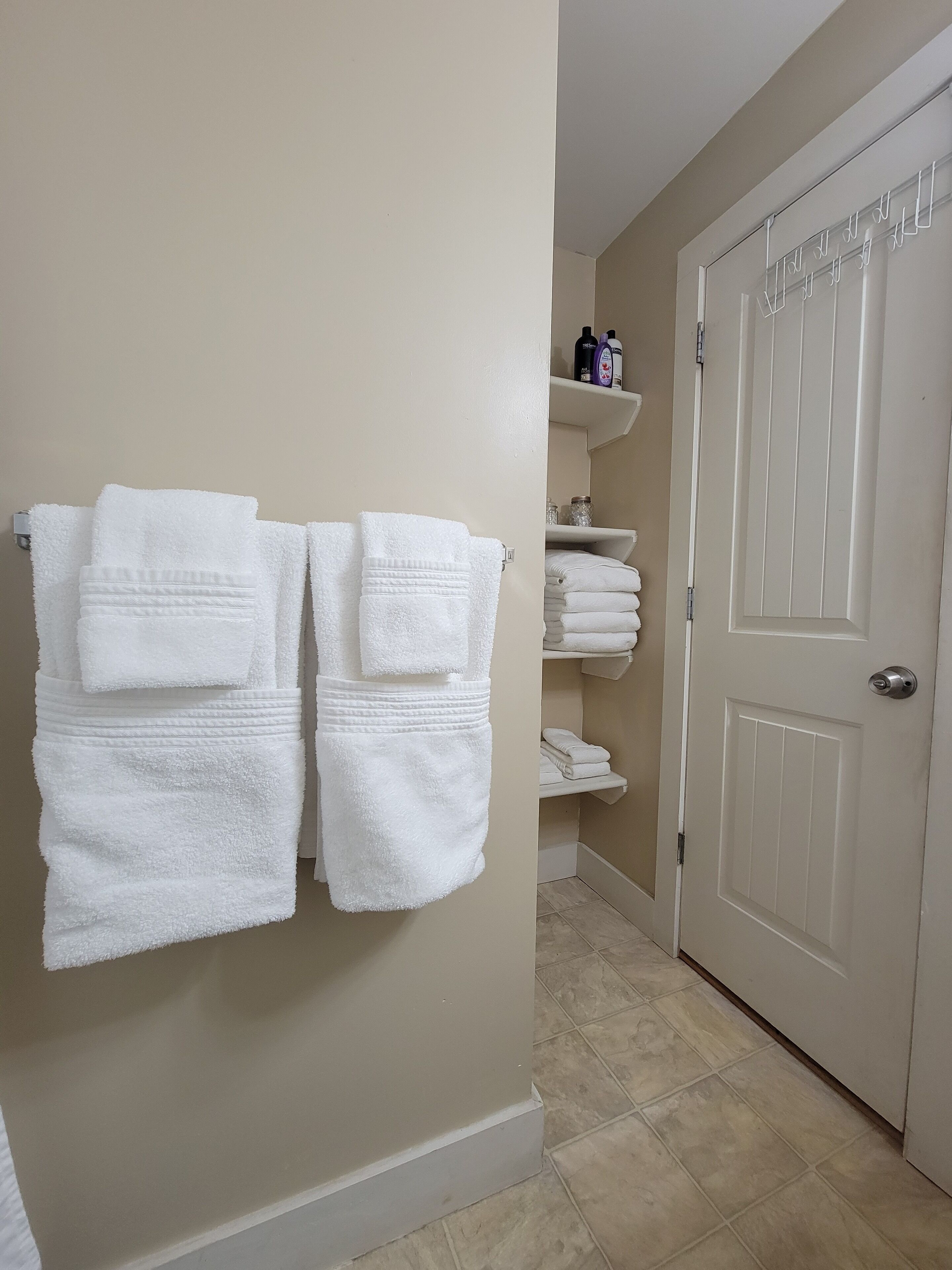 Une salle de bain avec des serviettes blanches suspendues à un porte-serviettes, une porte blanche et une étagère contenant des articles de toilette.