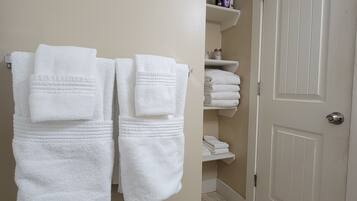 Une salle de bain avec des serviettes blanches suspendues à un porte-serviettes, une porte blanche et une étagère contenant des articles de toilette.