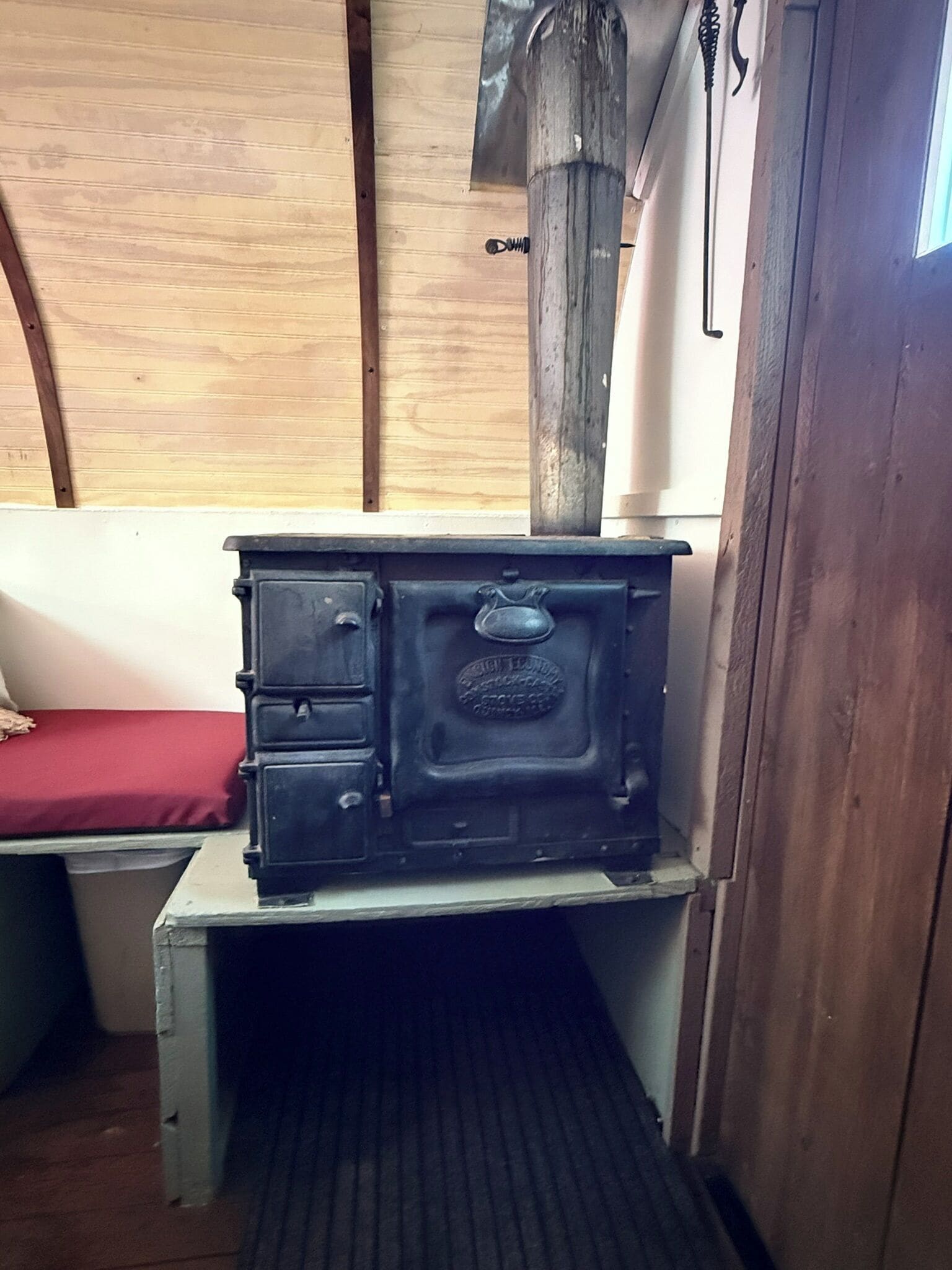 A compact room with a wooden bench, a small table with a black stove, and a wooden door.