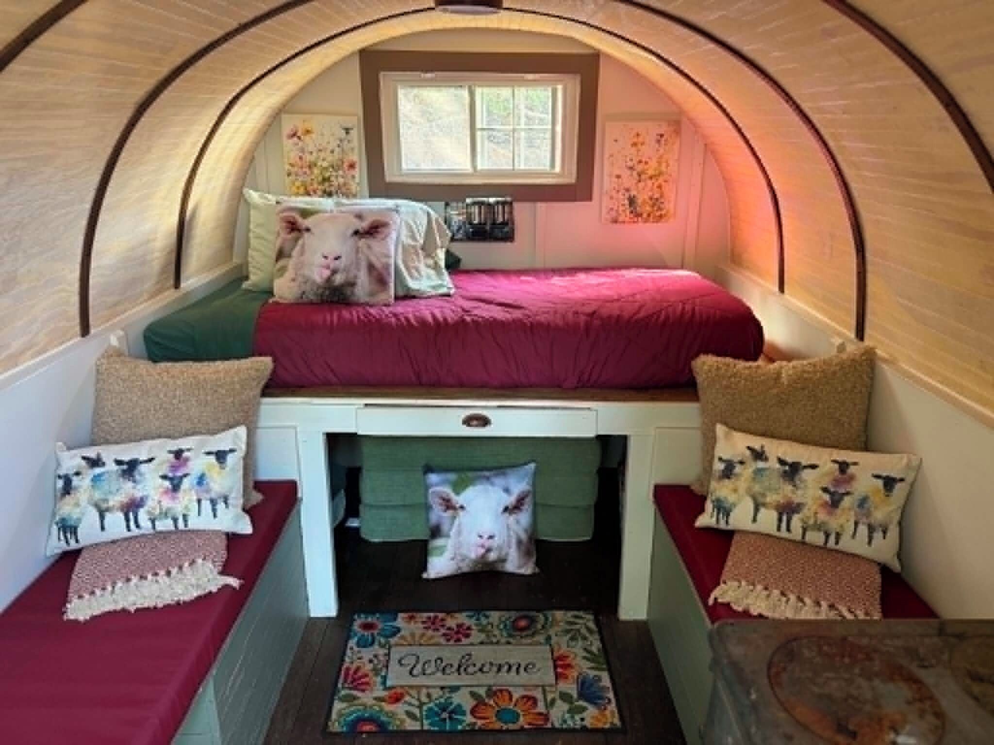A cozy interior with a bunk bed, a small table with a welcome mat, and decorative pillows.