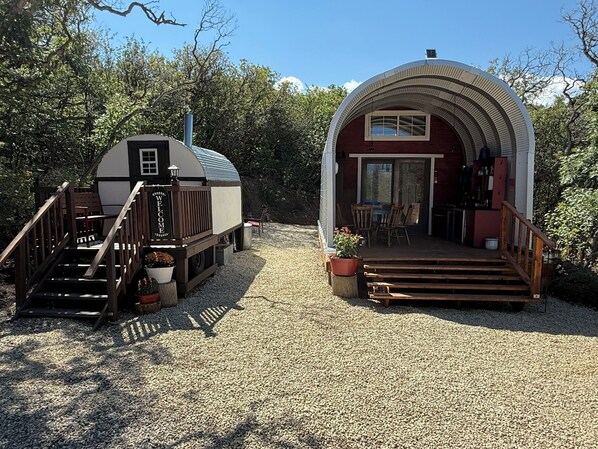 Une cabane rustique avec une pancarte accueillante, une véranda avec des marches en bois et une allée gravillonnée.
