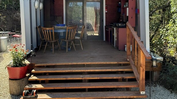 Une petite structure en forme d’arche, dotée d’une terrasse en bois, d’une table et de chaises devant.