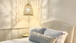 Una cama bien hecha con colcha blanca y dos almohadas, una mesita de noche con lámpara, y una pared con textura decorativa.