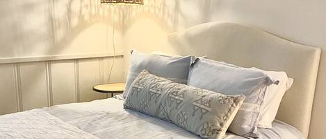 A neatly made bed with a white quilt and two pillows, a bedside table with a lamp, and a wall with a textured pattern.