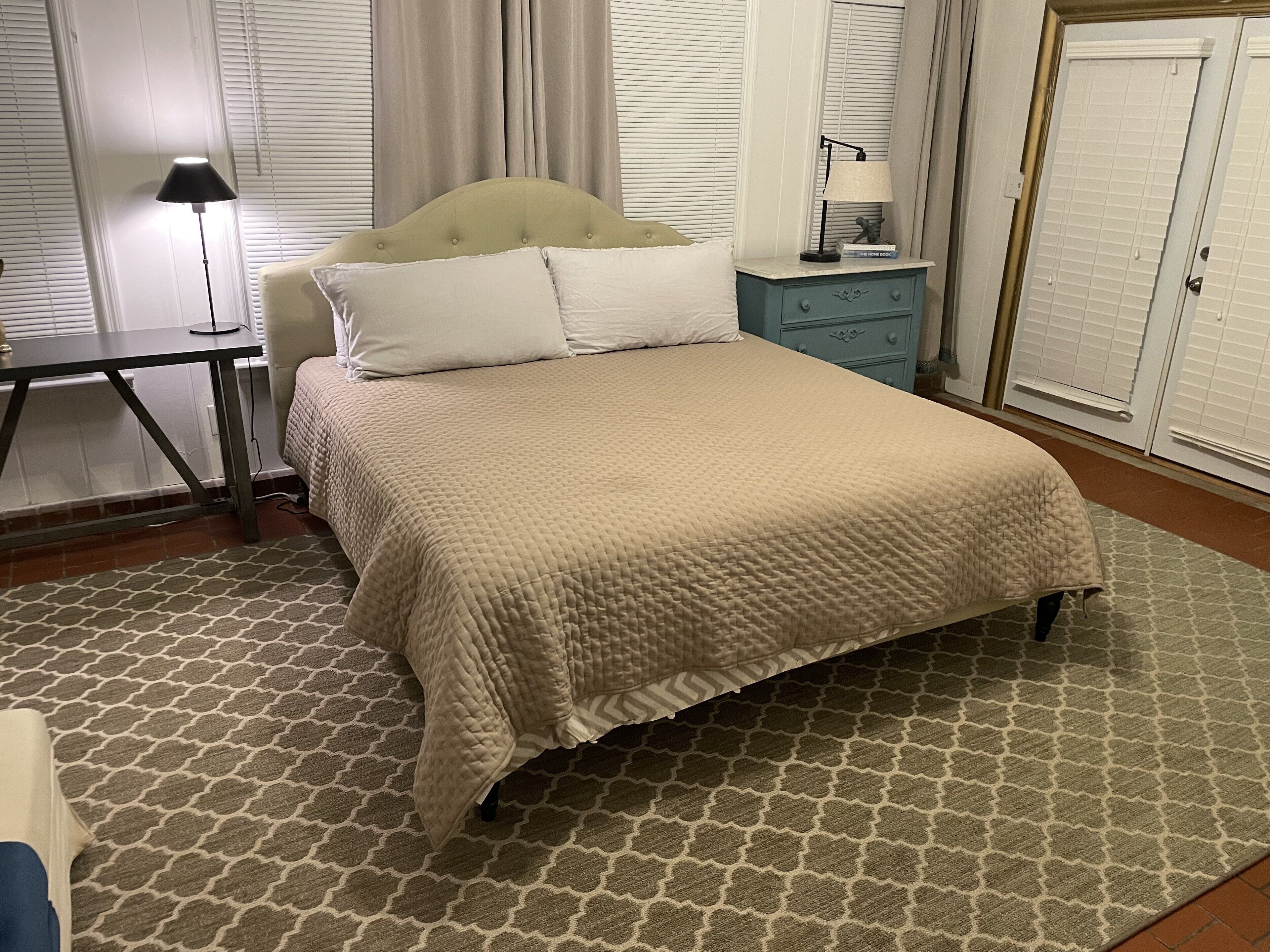 Un lit bien fait, recouvert d’une courtepointe matelassée, une table de chevet avec une lampe et un tapis à motifs.