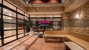 A spacious indoor area with a brick wall, large windows, and a seating area with a bench and a table. - ZONK HOTEL HAKATA (Fukuoka)