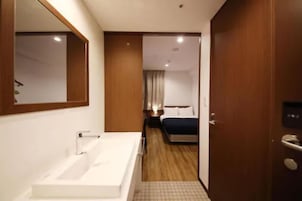 Quarto de hotel com uma banheira branca, uma porta de madeira e uma cama com colcha azul.