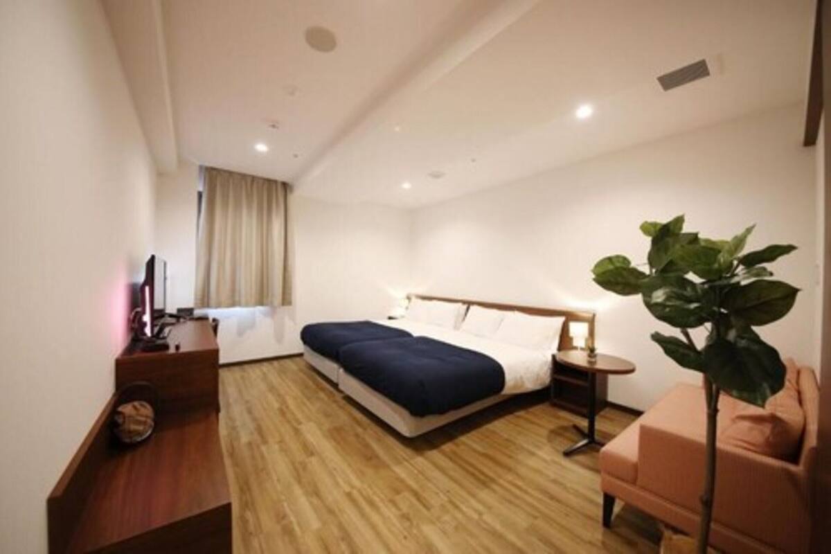 A hotel room with a bed, bedside table, chair, and a potted plant.