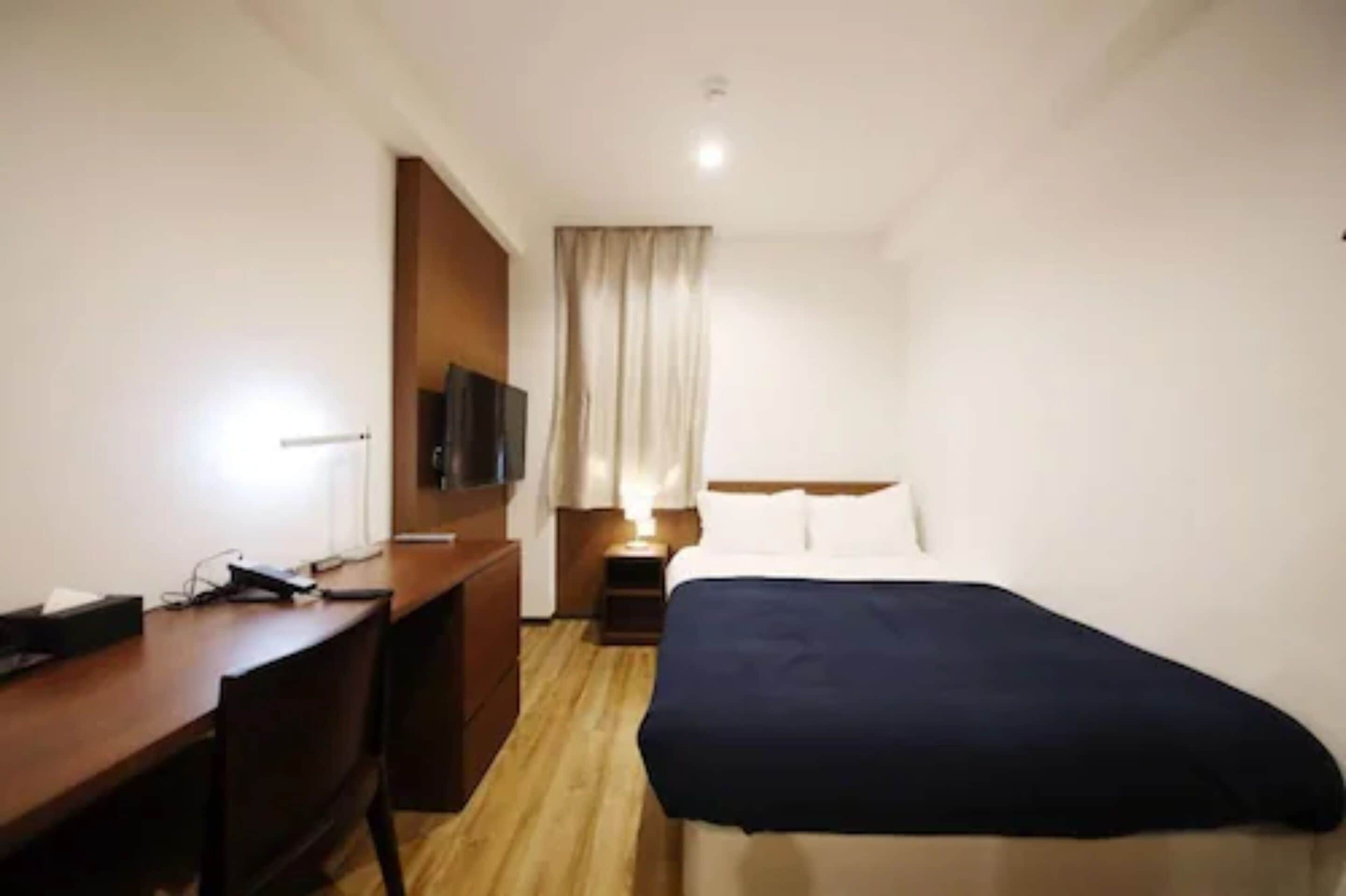 A hotel room with a bed, a desk, a television, and a window with curtains.