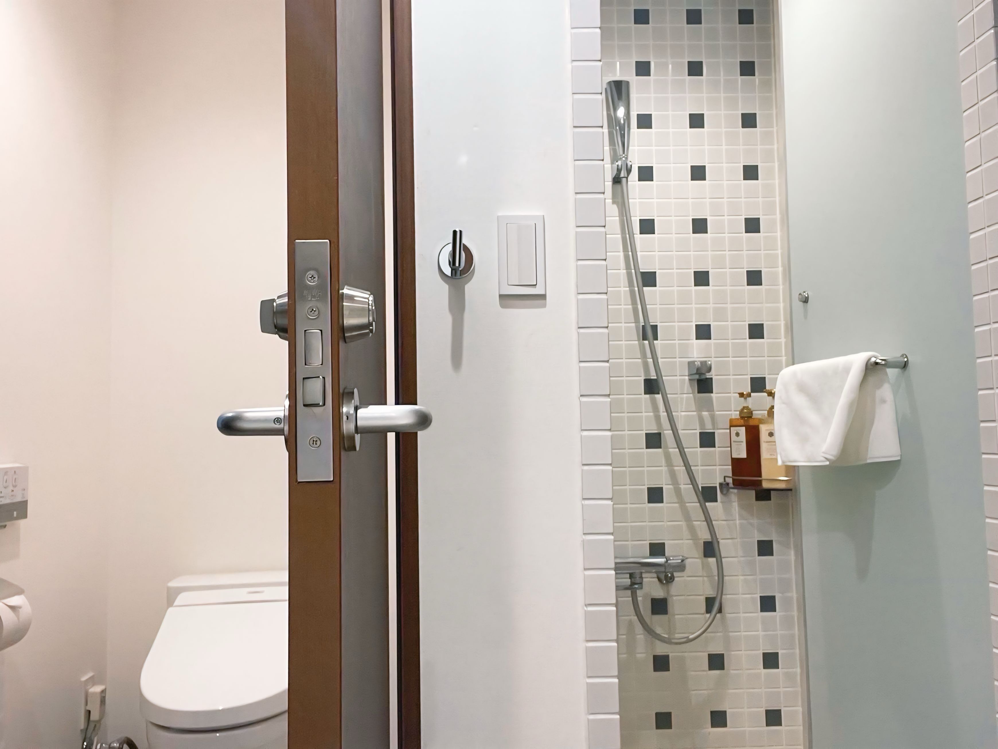 Un baño con inodoro, ducha con pared de azulejos y una toalla colgada en un perchero.