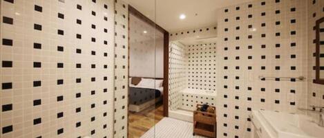 Une salle de bain avec des carreaux blancs et des touches noires, une baignoire, des toilettes et un petit banc en bois.