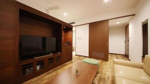 A modern living room with a flat-screen TV, wooden cabinets, a sofa, and a coffee table. - ZONK HOTEL HAKATA (Fukuoka)
