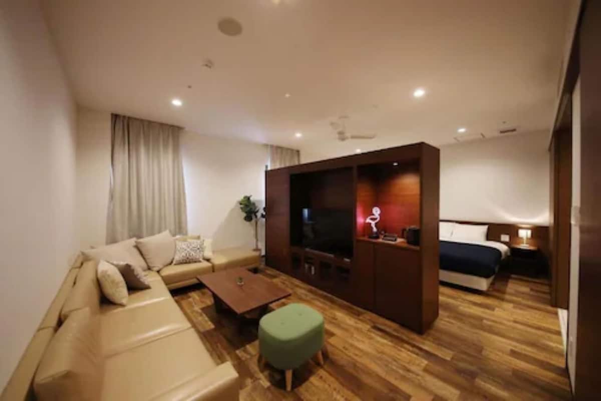 A modern hotel room with a sofa, a small table, a TV, and a bed.
