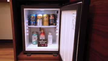 Un refrigerador lleno de diversas bebidas, incluyendo latas de cerveza y botellas de refresco.